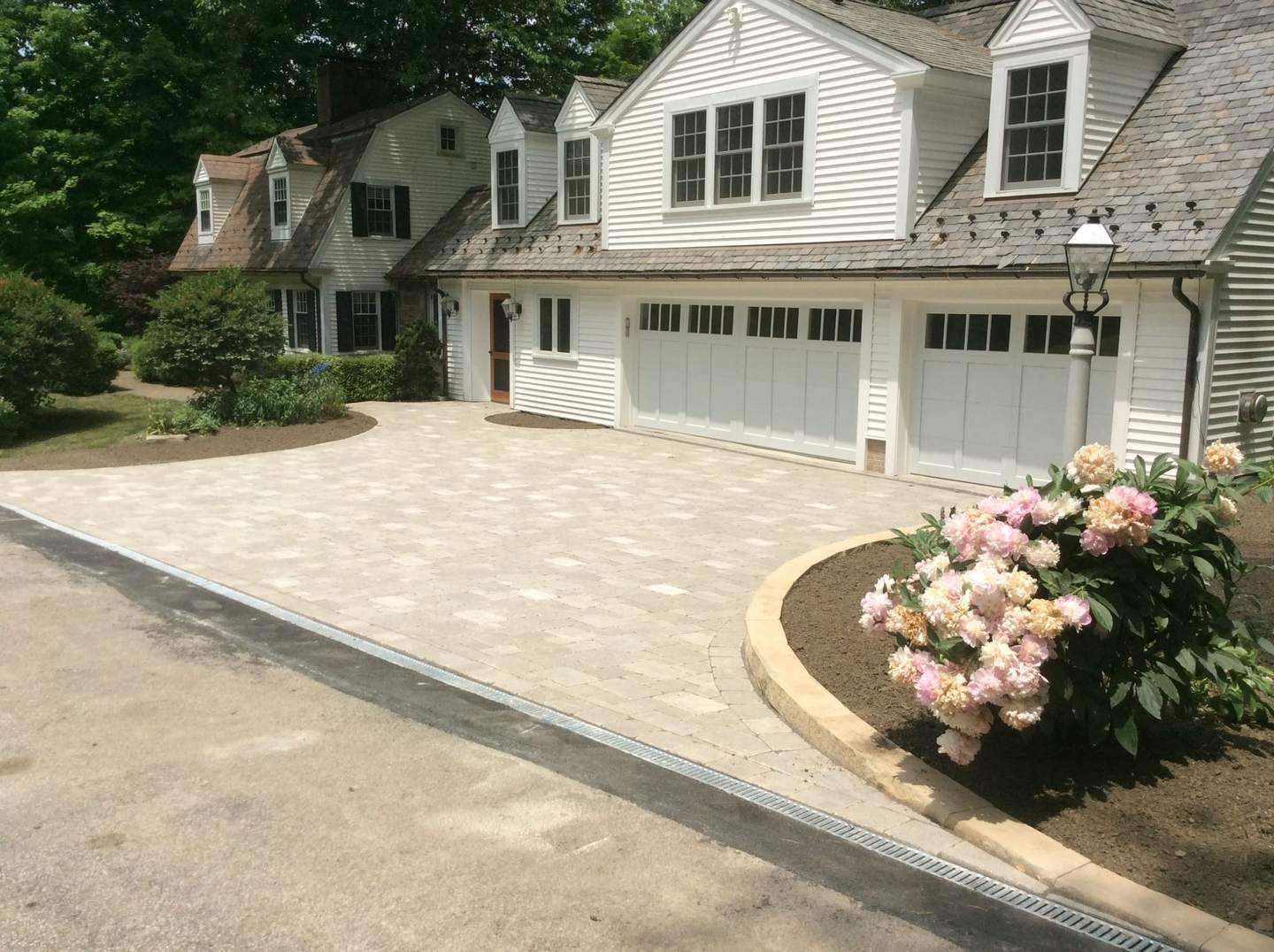 Paver driveway and landscaped garden bed beside a white home